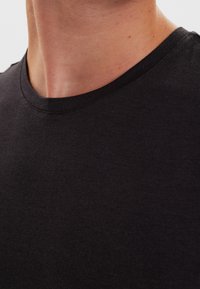 Czarny bawełniany t-shirt z okrągłym dekoltem, o gładkiej fakturze i równym wykończeniu. Szwy przy kołnierzu są minimalne.