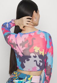 Top ajustado de manga longa em estampado de camuflagem translúcido, multicolorido, com acentos em azul, rosa e cinza. Apresenta um decote redondo e punhos costurados.