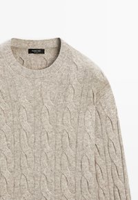 Beige Kabelstrickpullover aus weicher Wolle. Mit Rundhalsausschnitt und strukturiertem Muster mit hochstehenden, verflochtenen Kabeldetails.