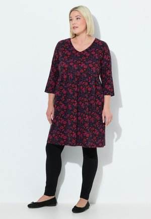 Blumenmusterkleid mit 3/4-Ärmeln, tiefem V-Ausschnitt und gerafftem Taillenbereich. Dunkler Hintergrund mit roten und blauen Blumen. Kombiniert mit schwarzen Leggings.