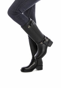 Botas de cuero negro hasta la rodilla con punta redonda, tacón de bloque medio, hebillas decorativas y acentos de remaches. Textura suave en todo su diseño.