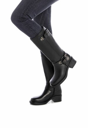 Botas de cuero negro hasta la rodilla con punta redonda, tacón de bloque medio, hebillas decorativas y acentos de remaches. Textura suave en todo su diseño.