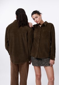 Bruine corduroy shirt met knoopsluiting, twee borstzakken en lange mouwen, gecombineerd met een minirok met luipaardprint en een bruine broek.