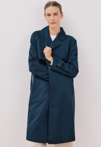 Marineblauer Trenchcoat mit durchgehender Knopfleiste, großen Revers und Seitentaschen. Glatte Stofftextur, mittellanges Design und taillierte Passform.