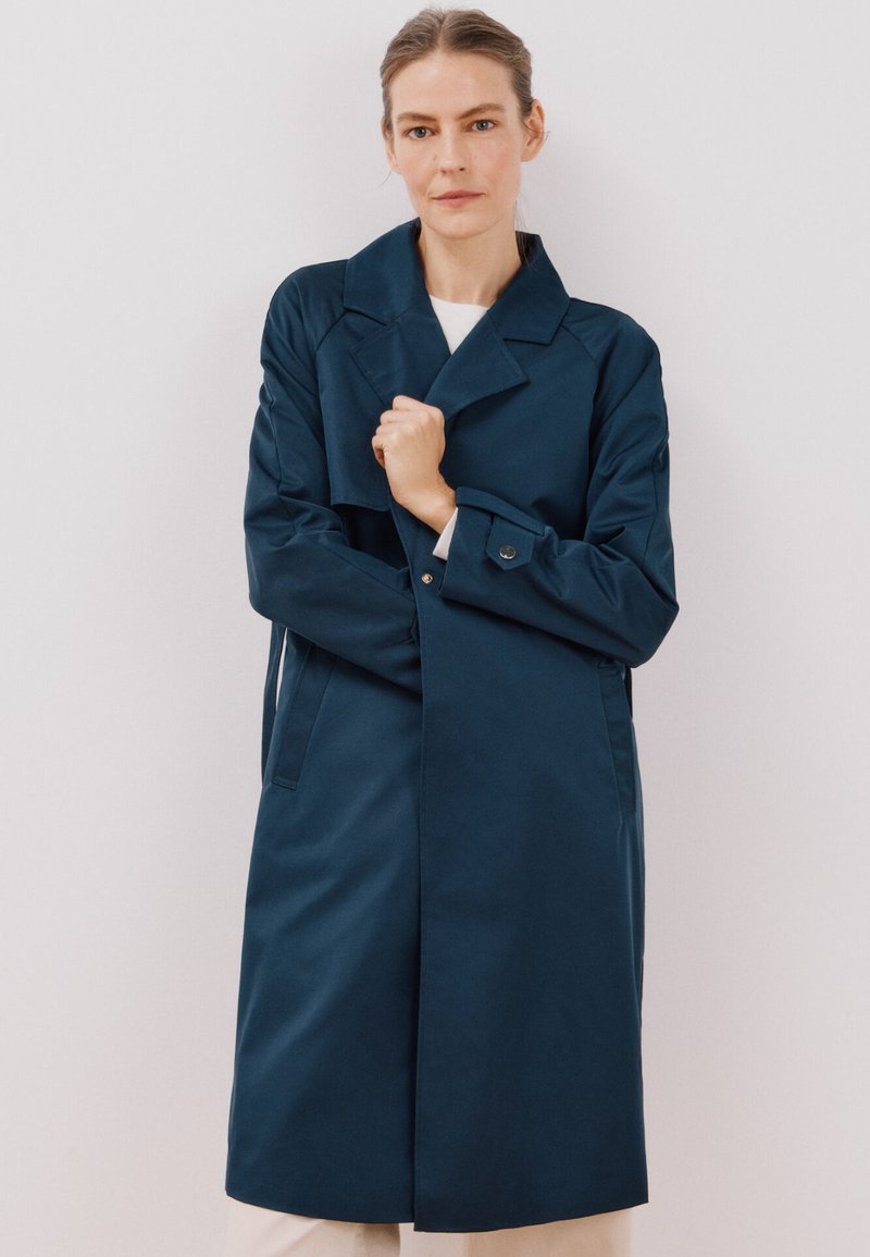 Marineblauer Trenchcoat mit durchgehender Knopfleiste, großen Revers und Seitentaschen. Glatte Stofftextur, mittellanges Design und taillierte Passform.