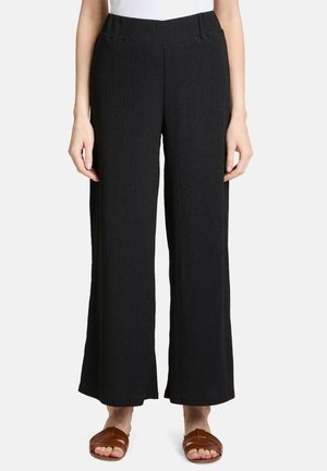 Pantalons larges noirs avec une texture côtelée et une ceinture élastique, présentant une coupe décontractée et une longueur raccourcie, associés à des sandales marron.