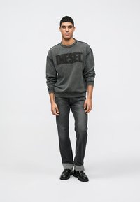 Sweatshirt cinza desbotado com logo "Diesel" em relevo, combinado com jeans escuros e sapatos pretos. Corte casual, mangas compridas, punhos enrolados.