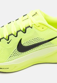 Nike juoksukengät, joissa on neonkeltainen verkko-otsikko, mustat yksityiskohdat, näkyvä logo, litteät nauhat ja pehmustettu pohja, jossa on "Zoom"-merkintä.