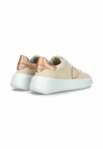 Beige sneakers med en tekstureret overflade og metalisk rosaguld-accenter på hælen. Hvid ydersål og minimalistiske designdetaljer.