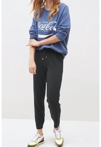 Modrá mikina s potiskem "Enjoy Coca-Cola", kombinovaná s černými joggingovými kalhotami a vícebarevnými sportovními botami s bílými, šedými a žlutými detaily.