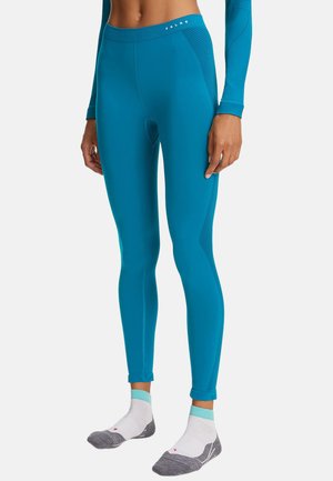Blaue nahtlose Leggings mit strukturierten Seitenpaneelen, getragen von einer stehenden Person mit passenden langen Ärmeln und weißen-grauen Knöchelsocken.