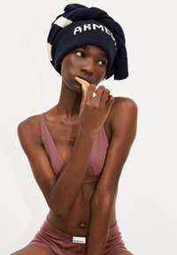 Maritiem gebreid beanie met witte letters "ARMED" en gestreepte accenten, gecombineerd met een mauve geribbelde beha en bijpassende shorts.