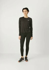 Camiseta atlética de manga larga negra con un logo, combinada con leggings negros y zapatillas negras con toques naranjas. Diseño suave y ajustado.