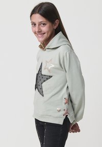 Sudadera verde menta con un gran diseño de estrella negra, capucha forrada con estampado de leopardo, detalles plateados y cordones laterales.