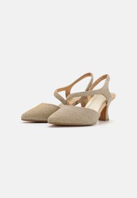 Talons aiguilles beiges à bride arrière avec une tige en tissu texturé, un bout pointu et un talon bloc mi-hauteur. Présente un design de bandoulière croisées.