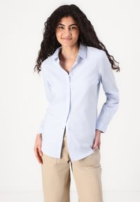 Cămașă butonată de un albastru deschis, cu dungi verticale albe; din bumbac; mâneci lungi; guler ascuțit; croială dreaptă. Pur și simplu peste pantaloni bej.