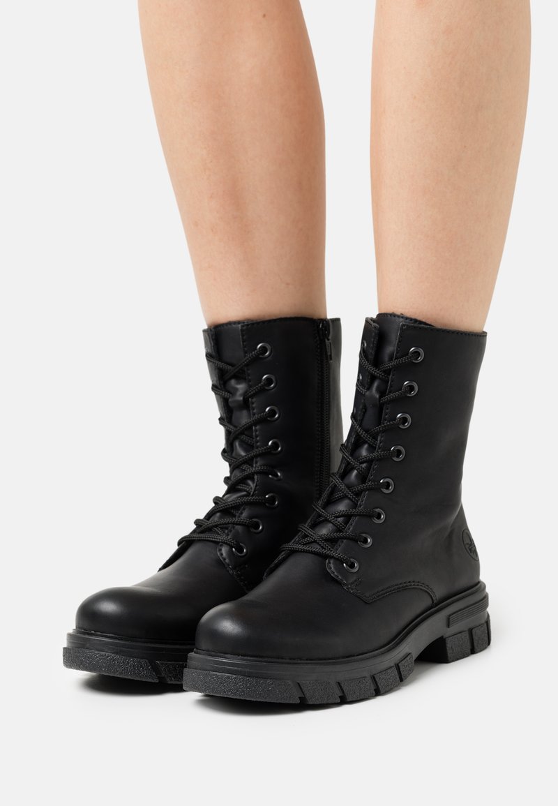 Botas de cuero negras hasta el tobillo con una puntera redonda, cierre de cordones en la parte delantera, cremallera lateral y suela de goma texturizada. Acabado liso y diseño minimalista.