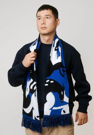 Dziany szalik z wzorem koni w kolorach niebieskim, czarnym i białym, z frędzlami na końcach i miękką fakturą. Noszony na szyi.
