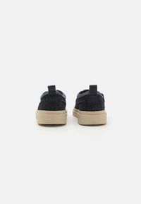Navy suede sneakers with a tan rubber sole, featuring a back pull tab and padded collar for support. Simple design with no visible patterns.