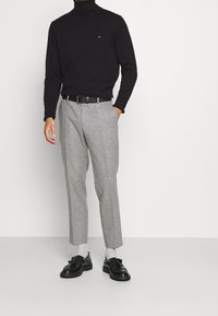 Czarny sweter z golfem, szare spodnie w kratę, czarny pasek i czarne eleganckie buty z frędzlami, do tego szare skarpetki.