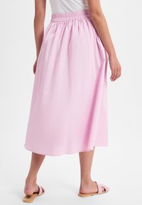 Hellrosa, knielanger Rock mit elastischem Bund und glatter Textur, getragen mit passenden rosa Riemchensandalen.