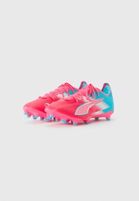 Un par de botas de fútbol en rosa y azul con acentos en blanco y plata y tachuelas moldeadas sobre un fondo blanco liso.