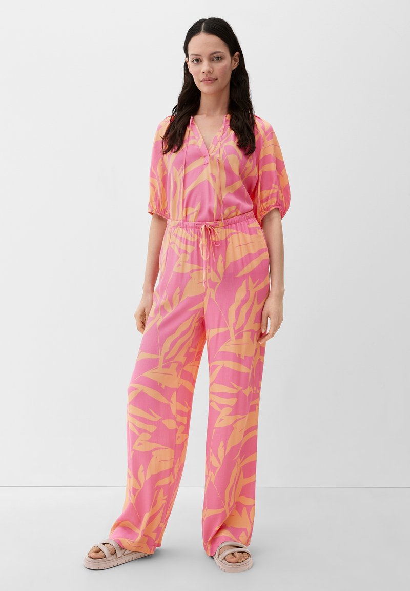 Rooie en oranje gestippelde jumpsuit met korte pofmouwen, een V-hals en een elastische taille. Heeft wijde benen en een gladde, lichte stof.