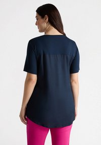 Top de color azul marino, de manga corta y con un acabado suave, cuenta con un dobladillo redondeado y un discreto detalle de costura en la parte posterior. Combinado con pantalones rosas.