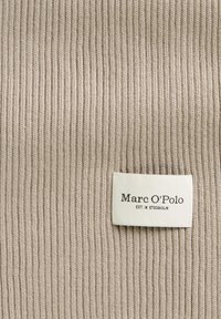 Beige ribbed knit fabric with a textured surface. White label featuring "Marc O'Polo" and "EST. IN STOCKHOLM" in black print.