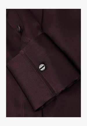 Manșetă de cămașă burgundy cu o textură netedă, având o închidere cu nasture și cusături contrastante de-a lungul marginii manșetei.