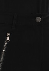 Schwarze Hose mit einem Reißverschlusstaschen-Detail und einem klassischen Knopfverschluss, mit einer glatten Textur und kontrastierenden Nähten.