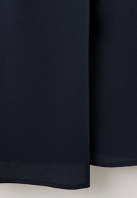 Tissu bleu marine foncé avec une couture verticale et une couture d'ourlet, montrant un léger pli sur un fond clair.