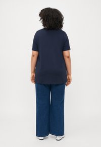 Marineblå, kortermet topp med rett snitt, parret med vid benjeans. Glatt tekstur, enkel design og standard søm.