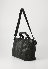 Black duffel bag made from textured material, featuring a zippered top, dual handles, and a detachable adjustable shoulder strap.