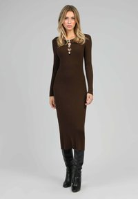 Robe longue en tricot côtelé marron à manches longues avec un col à boutons, associée à des bottes noires à talons hauts jusqu'aux genoux. Texture lisse, silhouette ajustée.