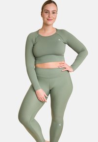 Rippierter langärmliger Cropped-Top und hochgeschnittene Leggings in Salbeigrün, mit einem figurbetonten Design und einem kleinen Logo an der Seite der Leggings.