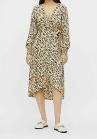 Sukienka typu wrap z lekkiego materiału, w kwiatowy wzór z żółtymi, purpurowymi i czarnymi akcentami. Dekolt w serek, długie rękawy, asymetryczny dół.