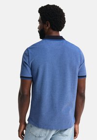 Modrá polo tričko s texturovanou tkaninou, krátkými rukávy a kontrastním tmavě modrým límcem, s modrými akcenty na lemech rukávů.