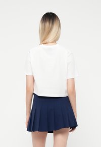 Hvit avkortet t-skjorte parret med et plissert marineblått skjørt. T-skjorten har korte ermer og en enkel rund halslinning. Glatt stoffstruktur.