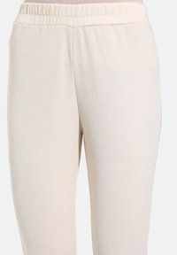 Gestreepte lichtbeige broek met een elastische tailleband, met een zachte textuur en een taps toelopende pasvorm, ontworpen voor comfort en draaggemak.