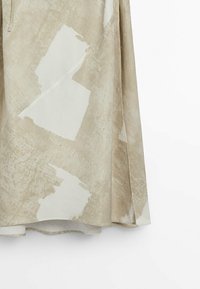 Jupe beige en tissu léger avec des motifs abstraits en crème et tan. Présente un design fluide et un ourlet courbé distinctif.