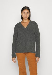 Gray knitted sweater with a V-neck, relaxed fit, and ribbed cuffs, paired with orange corduroy pants. Soft texture, casual design.