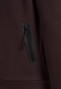 Nahaufnahme eines schwarzen vertikalen Reißverschlusses mit zwei Zippern auf dunkelbraunem Stoff, die den Reißverschluss und die Textur hervorhebt.