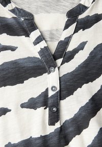 Zwart-wit gestreepte top met zebra-print, voorzien van een V-hals, drie knopen aan de voorkant, zachte textuur en contrasterende stiksels.