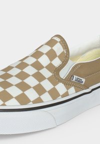 Ταμπά και λευκό καρό slip-on αθλητικό παπούτσι Vans με λευκή λαστιχένια σόλα και ορατές ραφές, φαίνεται από το πλάι σε απλό φόντο.