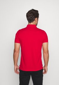 Chemise polo rouge à manches courtes avec un col, texture lisse et design ajusté. La vue arrière montre des lignes épurées et un minimum de détails.