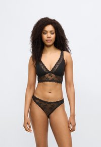 Mustasta pitsistä valmistettu rintaliivit, joissa on kukkakuvio ja aaltoileva reunus, yhdistettynä mustiin pitsisiin bikinihousuihin. Läpinäkyvä materiaali, V-pääntie.