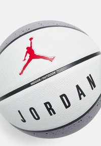 Witte basketbal met een gestructureerd oppervlak, rood Jordan-logo, zwarte accenten en een label "INDOOR/OUTDOOR", met een strak ontwerp.