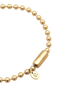 Armbands av gulledade pärlor med en serie släta, runda pärlor och ett ovalt metallspänne med en ingraverad logocharm.