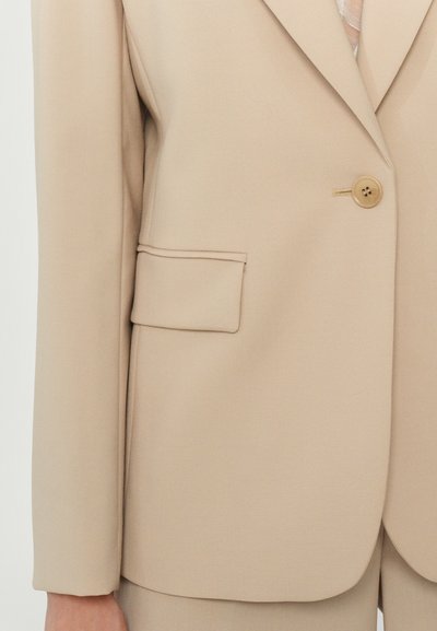 Beige blazer met een enkele knoopsluiting, gestructureerde schouders en een opgestikte zak. Soepele stof met een matte afwerking.